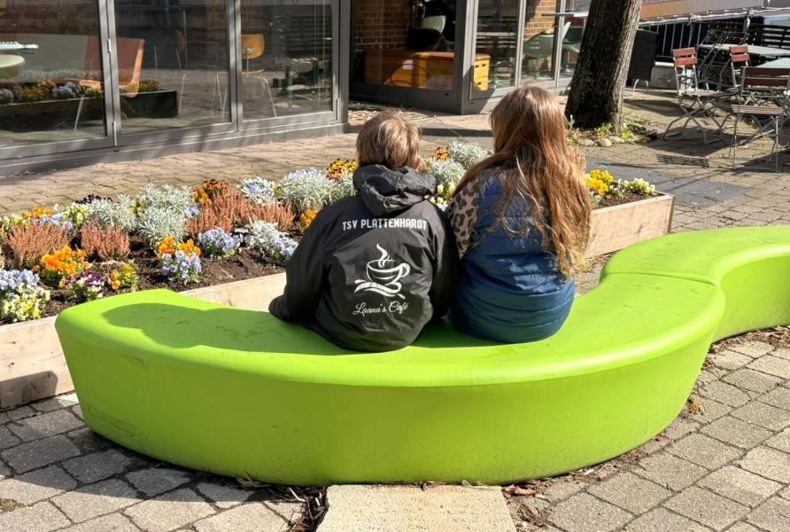 Zwei Kinder sitzen auf den grünen Bänken