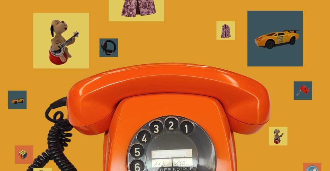 Motiv zur Ausstellung "Die 70er Jahre". Orangefarbenes Telefon und weitere Objekte, wie Zauberwürfel und Modellauto