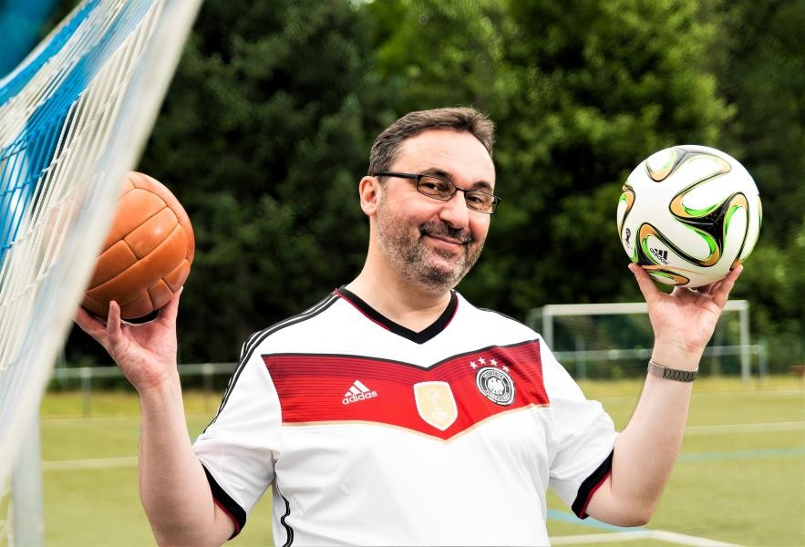 Mann in Fußballtrikot mit einem Ball in jeder Hand