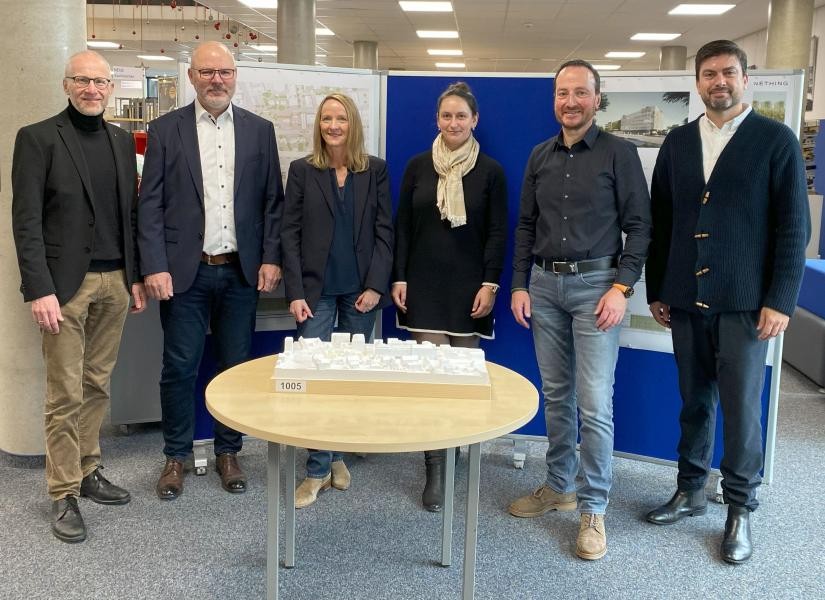 Die Genannten in der Bibliothek vor dem Modell, das auf einem Tisch steht.