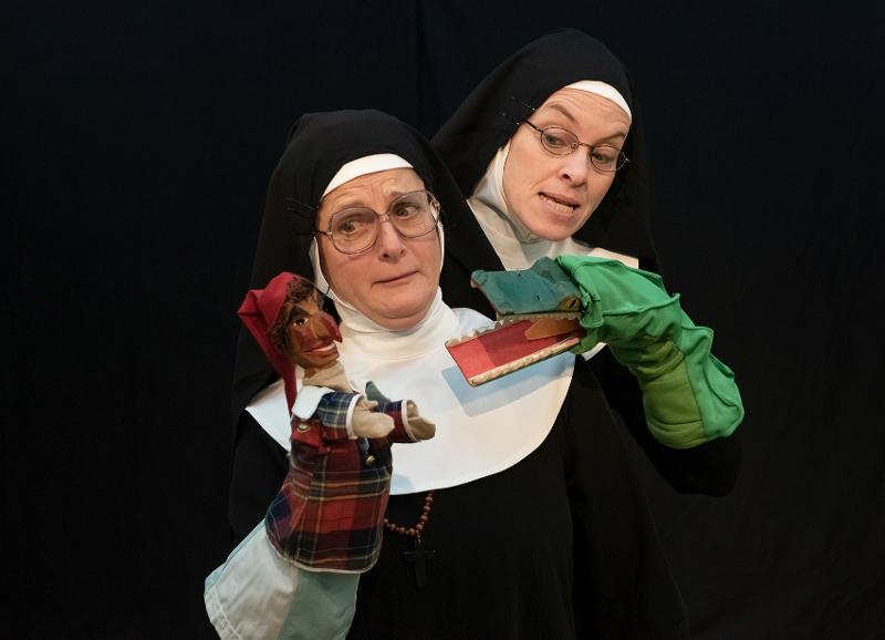 Zwei Frauen sind wie Nonnen verkleidet und halten in ihren Händen Handpuppen