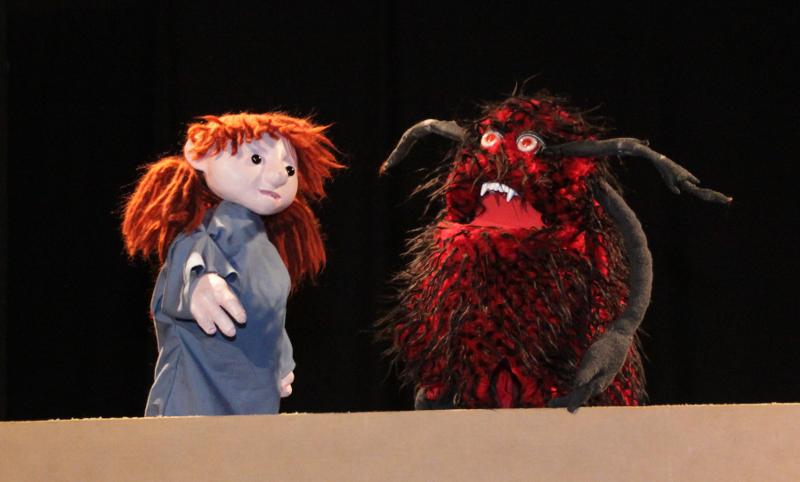 Eine rothaarige Mädchen-Puppe steht gegenüber eines rot-schwarzen Zottelmonsters (Puppe)