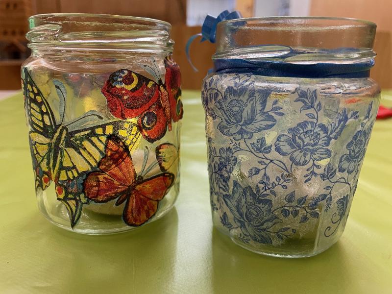 Zwei selbst gestaltete Windlichter, Gläser mit aufgeklebten Motiven (Schmetterlinge und Blumen)