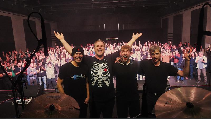 Auf dem Bild steht die Band auf der Bühne im Hintergrund ist das Publikum zu sehen