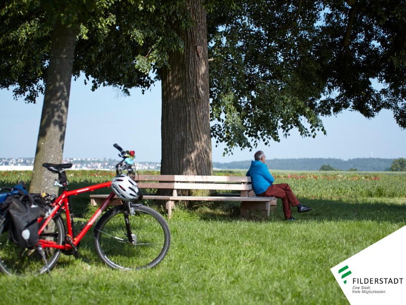 Ein Mann sitzt unter einem Baum. Im Vordergrund steht sein rotes Fahrrad